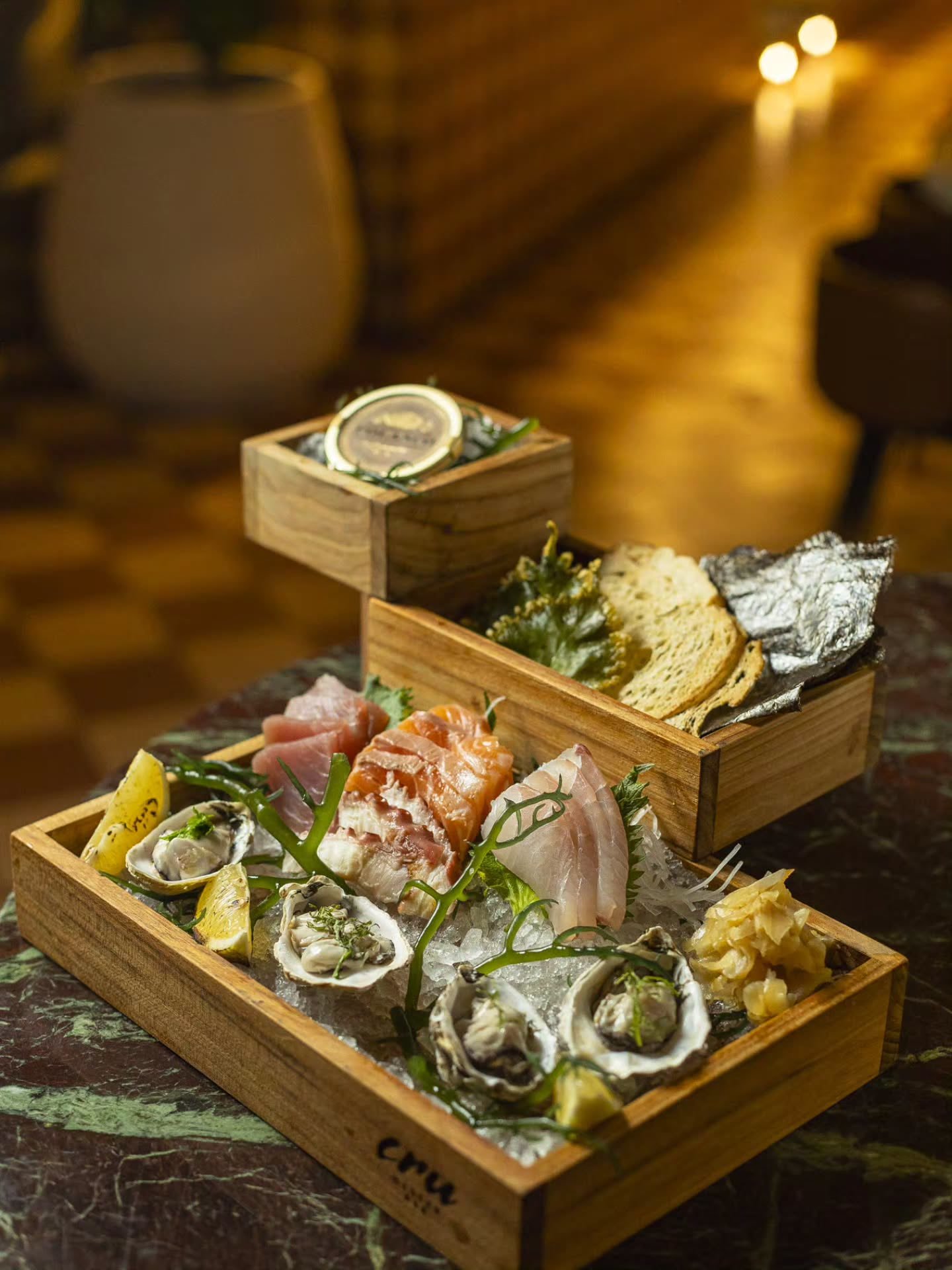Plateau com ostras, sashimis de atum, salmão e peixe branco no gelo, caviar e torradas em caixas de madeira