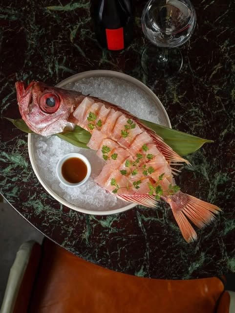 Peixe vermelho inteiro fatiado em sashimi sobre gelo, com molho ponzu ao lado